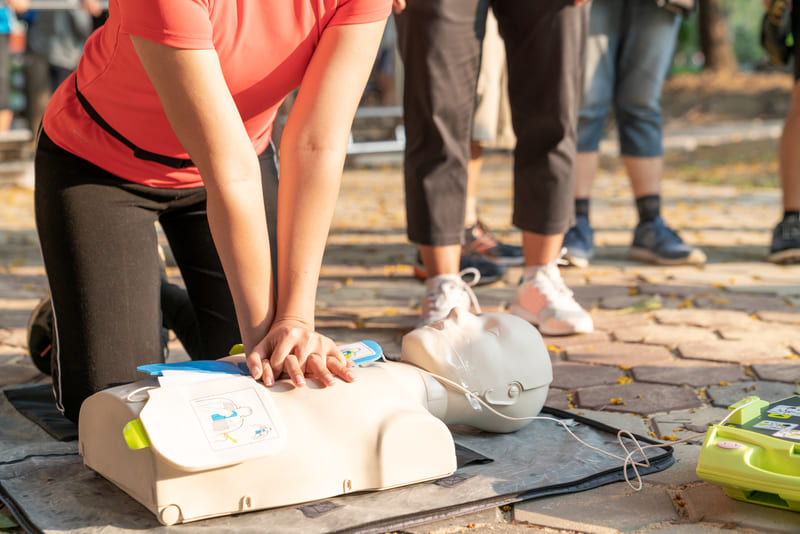 first-aid-course-asian-female-or-runner-woman-training-cpr-demonstrating-class-in-park-by-put-hands-and-interlock-finger-over-cpr-doll-give-chest