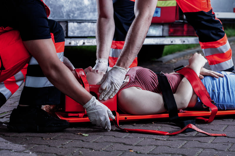 first-aid-training-medical-rescuer-bending-over-a-car-accident-victim-lying-on-a-stretcher